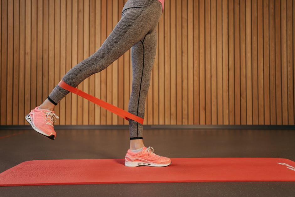 A woman performing leg exercises using a red resistance band on a yoga mat indoors.
